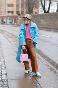 chica en la calle viste piezas de diferentes colores pastel, un abrigo, bolso, vaqueros, t shirt y tennis