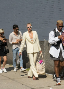 Chica blanca haciendo fila en una calle de Nueva York viste un traje completo color blanco roto y usa gafas de sol