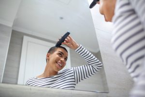 chica frente a espejo se rapa la cabeza con maquina de afeitar como resultado de tratamiento oncologico