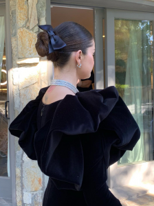 Actriz Selena Gomez aparece de espaldas con un moño de bailarina con lazo mientras viste un vestido negro y un collar de diamantes