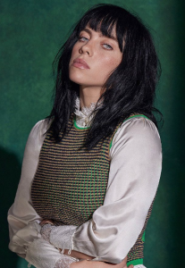 Cantante Billie Eilish aparece con una blusa blanca y un chaleco tejido verde con un look de cabello peinado despeinado sobre un fondo verde