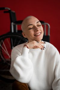 chica con cabeza rapada sonríe frente a un fondo rojo y silla de ruedas emulando ser paciente de tratamiento oncologico