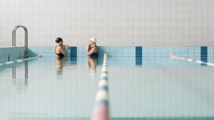 dos mujeres dentro de una piscina techada están frente a frente platicando después de haber terminado una sesión de balmeoterapia
